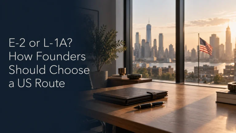 Founder desk by a tall window in a modern American office with a US city skyline and an American flag beyond, illustrating the choice between an E-2 and an L-1A visa for founders.